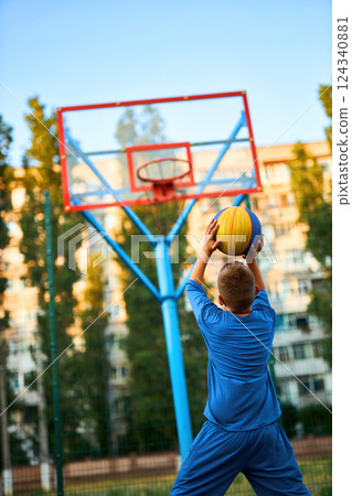 The rear view of a young boy shooting a basketball toward a hoop. The rear view of a young boy shooting a basketball toward a hoop. 124340881