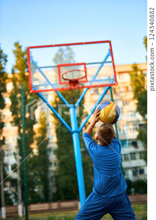 The rear view of a young boy shooting a basketball toward a hoop. 124340882
