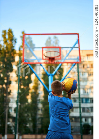 The rear view of a young boy shooting a basketball toward a hoop. 124340883