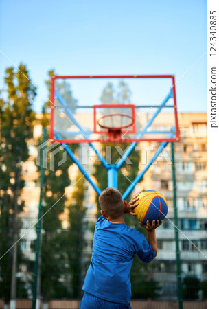 The rear view of a young boy shooting a basketball toward a hoop. 124340885