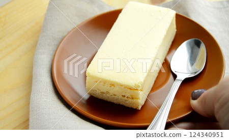 Laying out a brown plate with a rectangular slice of delicious cheesecake close-up on the table Laying out a brown plate with a rectangular slice of delicious cheesecake close-up on the table 124340951