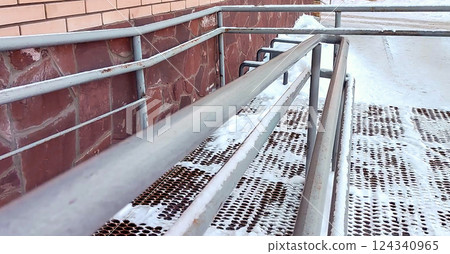 Close-up of a ramp with metal railings, covered with snow, for baby strollers and handicapped accessibility 124340965