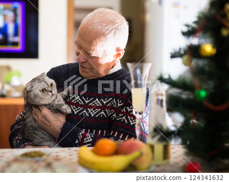 Happy elderly man together with a cat of the Scottish breed celebrates the new year at festive table Happy elderly man together with a cat of the Scottish breed celebrates the new year at festive table 124341632