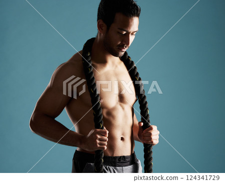 Body, fitness and rope with man in studio for exercise, training or workout routine. Equipment, health and muscular with shirtless model on blue background for challenge, performance or power 124341729
