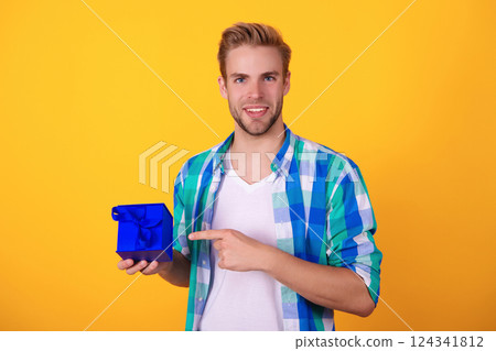 Birthday gift. Party on mens day. Mens day. Birthday party present. Man pointing finger. Young guy hold present box for Valentines day. Happy anniversary. Man with gift isolated on yellow 124341812