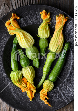 Top view on fresh zucchini with flowers on black plate close up Top view on fresh zucchini with flowers on black plate close up 124342926
