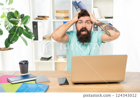Surprised man with jaw dropped clutching head sitting at laptop in office, surprise Surprised man with jaw dropped clutching head sitting at laptop in office, surprise 124343012