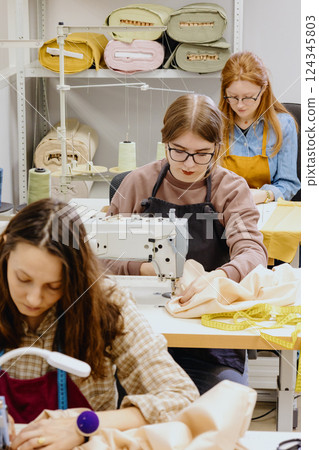 Three women sew in workshop at clothing factory. industrial equipment sewing machines. 124345803