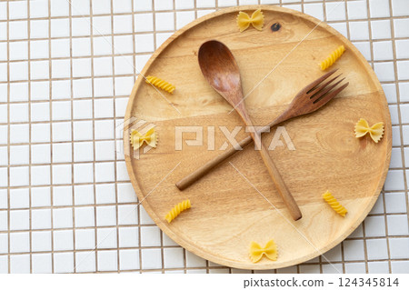 time to eat pasta. wooden plate with fork and spoon in form of clock hands. pasta on plate. time to eat pasta. wooden plate with fork and spoon in form of clock hands. pasta on plate. 124345814