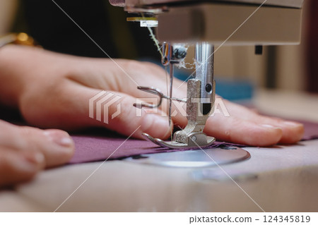 woman sews piece of cloth on sewing machine. industrial metal machine for all fabric tops.  124345819