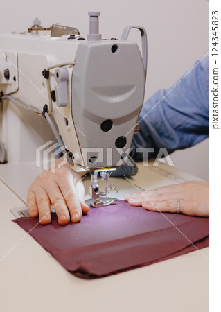 woman sews piece of cloth on sewing machine. industrial metal machine for all fabric tops.  124345823