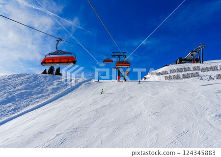 Skiers on a chairlift in the Austrian Alps enjoy the view of the snow-covered mountains. 124345883