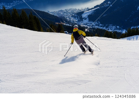 Skier glides down a snowy slope with a beautiful mountain and town in the distance Skier glides down a snowy slope with a beautiful mountain and town in the distance 124345886