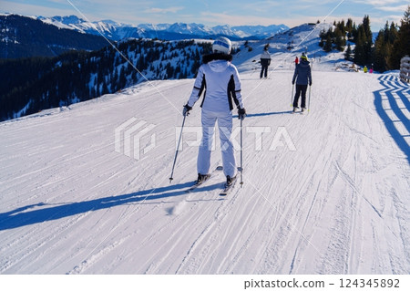 Skier Dressed in White Outfit Skillfully Glides Down the Snowy Mountainside Surrounded by Trees 124345892