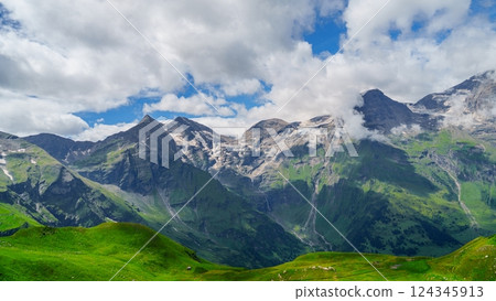 Green mountains with snow-covered peaks and a blue sky with white clouds Green mountains with snow-covered peaks and a blue sky with white clouds 124345913