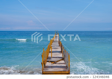 The old wooden pier goes into the horizon of the incredible azure color of the ocean. 124346046