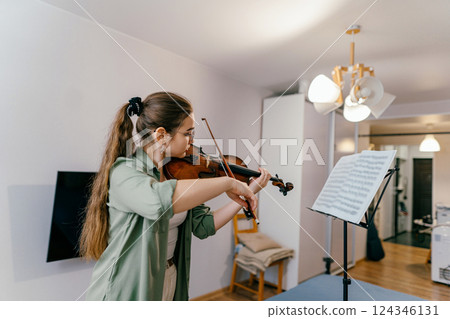 Young girl student playing violin and learning musical composition from sheet music. A young musician refines her skills through focused classical music practice. 124346131