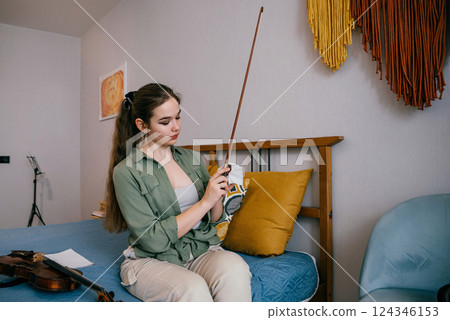 Focused young woman applying rosin to a bow as part of instrument preparation. A professional musician prepares her bow for rehearsal by fine-tuning its grip and response 124346153