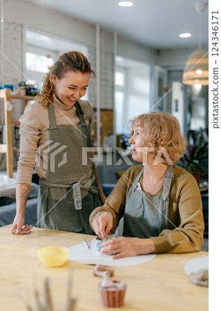 Elderly Caucasian woman learns pottery at a creative workshop with a young mentor. Two women work together with clay, developing skills and enjoying the artistic process 124346171