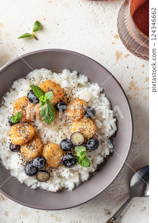 Rice porridge with banana, blueberries, chia seeds and honey sauce on a table close up, hot and healthy breakfast 124346662