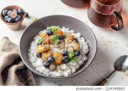 Rice porridge with banana, blueberries, chia seeds and honey sauce on a table, hot and healthy breakfast Rice porridge with banana, blueberries, chia seeds and honey sauce on a table, hot and healthy breakfast 124346663