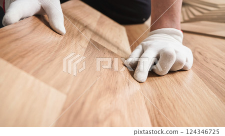Installing laminated floor, detail on man hands in white gloves fitting wooden tiles 124346725
