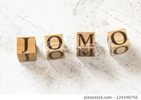 Four wooden cubes with letters JOMO (meaning Joy of missing out) on white working board. Four wooden cubes with letters JOMO (meaning Joy of missing out) on white working board. 124346756