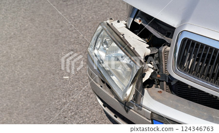 Crashed car, detail on front headlight, glass not broken, hanging from dented bumper plates Crashed car, detail on front headlight, glass not broken, hanging from dented bumper plates 124346763