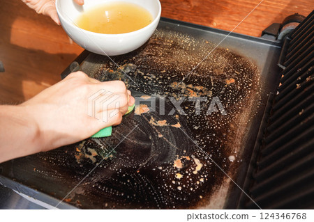 Cleaning electric grill dirty plate with soaped sponge, detail on woman hand Cleaning electric grill dirty plate with soaped sponge, detail on woman hand 124346768