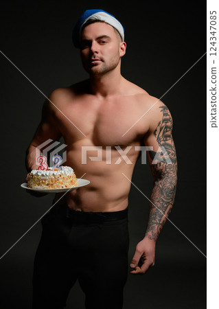 Celebrating a birthday with a muscular athlete and a cake in a dark setting 124347085