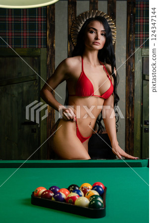 Woman posing in red lingerie beside a green pool table in a stylish interior 124347144