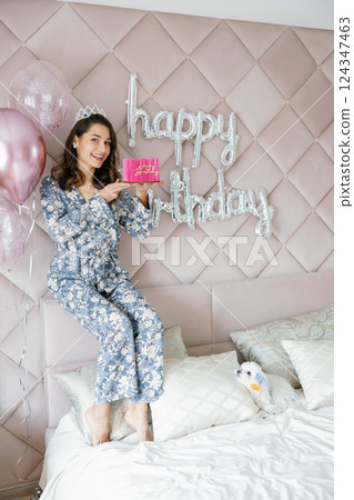 Woman celebrating birthday holding pink cake with balloons and happy birthday sign 124347463
