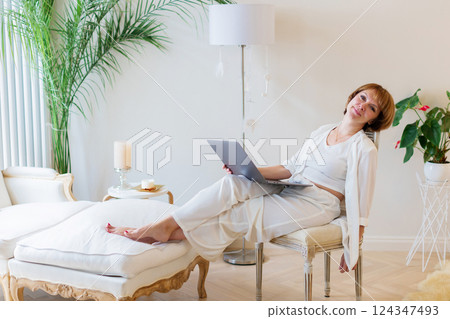 Senior stylish woman sitting with her laptop and making a pause in working day at home. Adult freelancer is tired and make a pause while working on laptop in living room. 124347493