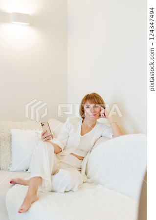 Adult beautiful woman relax siting on sofa at home and using cellphone texting chatting with friend. Happy young woman on couch holding smartphone in her hands, shoping online or check social media. 124347494
