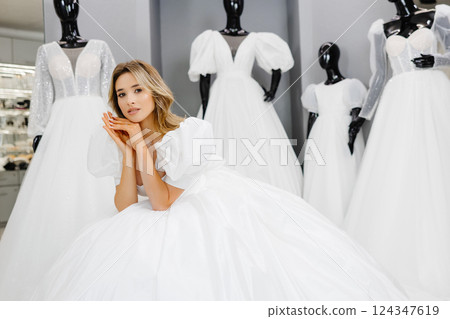 Pretty young woman is choosing a wedding dress in the shop. The bride-to-be is wearing a wedding dress for fitting 124347619