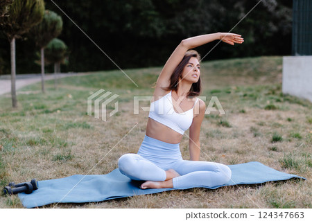 Young woman practicing yoga stretching in park on a mat 124347663