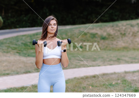 Young woman lifting weights during outdoor workout in a park Young woman lifting weights during outdoor workout in a park 124347669