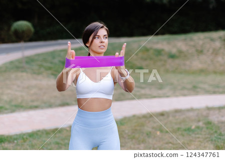 Fitness model exercising with resistance band in a park Fitness model exercising with resistance band in a park 124347761