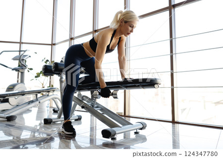Athletic woman lifting dumbbell during workout in gym 124347780