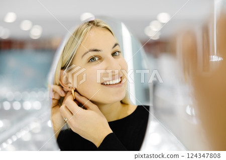Happy woman trying on gold earrings in jewelry store Happy woman trying on gold earrings in jewelry store 124347808