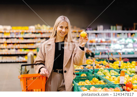 Woman holding apple and shopping basket buying groceries at supermarket 124347817
