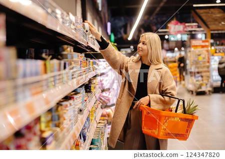 Customer picking groceries from supermarket shelf with shopping basket 124347820