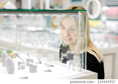 Woman looking on jewelry behind glass display in a store 124347857