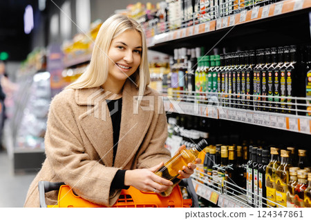 Smiling woman choosing olive oil in supermarket, holding a bottle and shopping cart Smiling woman choosing olive oil in supermarket, holding a bottle and shopping cart 124347861
