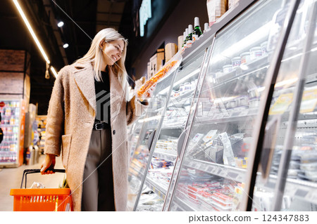 Woman choosing packaged food from refrigerated section in supermarket Woman choosing packaged food from refrigerated section in supermarket 124347883