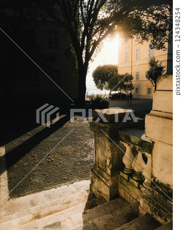 Sun shining through trees, illuminating stone stairs and railing. Warm sunlight filters through leaves of trees, casting golden glow on stone staircase and railing, creating a picturesque urban scene Sun shining through trees, illuminating stone stairs and railing. Warm sunlight filters through leaves of trees, casting golden glow on stone staircase and railing, creating a picturesque urban scene 124348254
