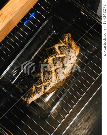 Fish baking with aromatic herbs and spices in glass container inside oven, highlighting nutritious, appetizing cooking method for healthy meals. Fish baking in container in oven. First-person view 124348278