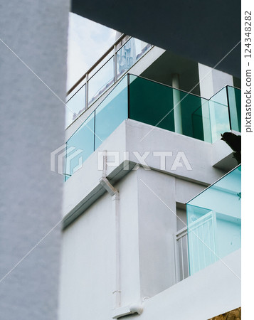 Modern building. Low angle view capturing a modern white building featuring sleek glass balconies and a clean white rain gutter, highlighting innovative architectural design and urban elegance 124348282
