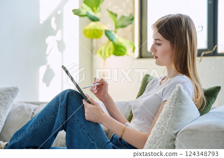 Young woman using digital tablet sitting on sofa at home 124348793