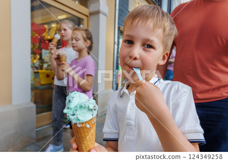 Portrait cute cheerful child enjoy ice cream walk together with family at european city street road on hot summer sunny day. Funny kids eat sweet vanilla icecream walking outdoors Portrait cute cheerful child enjoy ice cream walk together with family at european city street road on hot summer sunny day. Funny kids eat sweet vanilla icecream walking outdoors 124349258